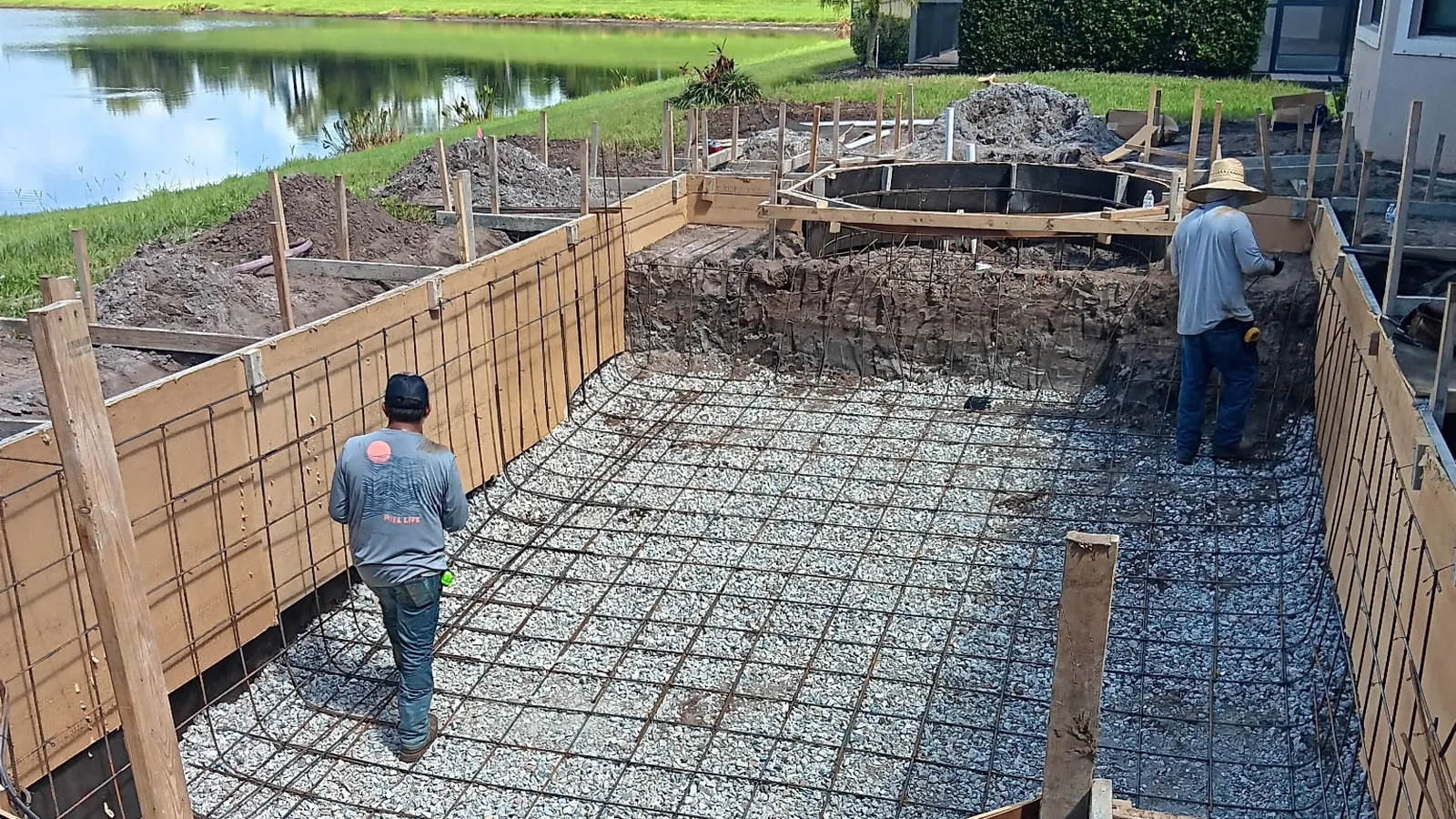 Crew tying the rebar grid inside a formed pool shell beside a lake