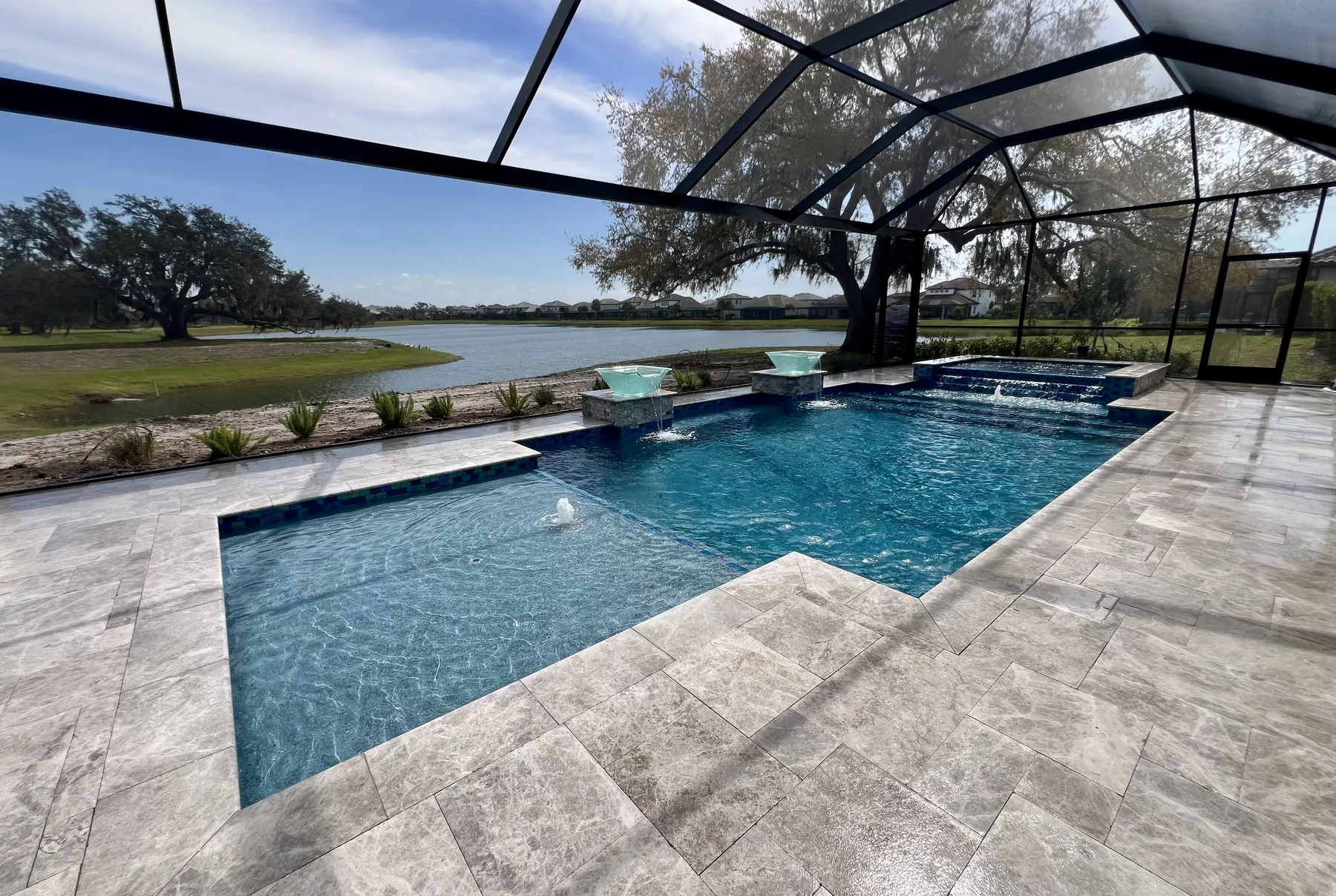 Finished pool and travertine deck looking out to a lake and oak tree