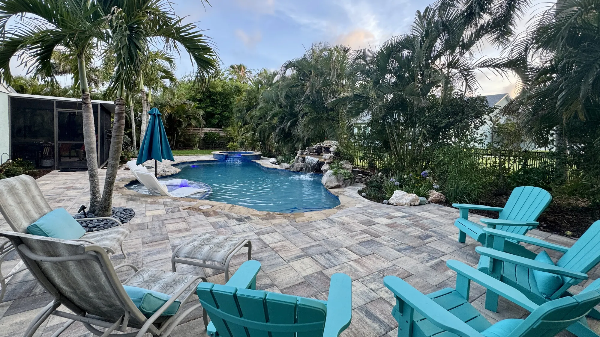 Freeform pool with a rock grotto, palms and turquoise chairs on a paver deck in Bradenton