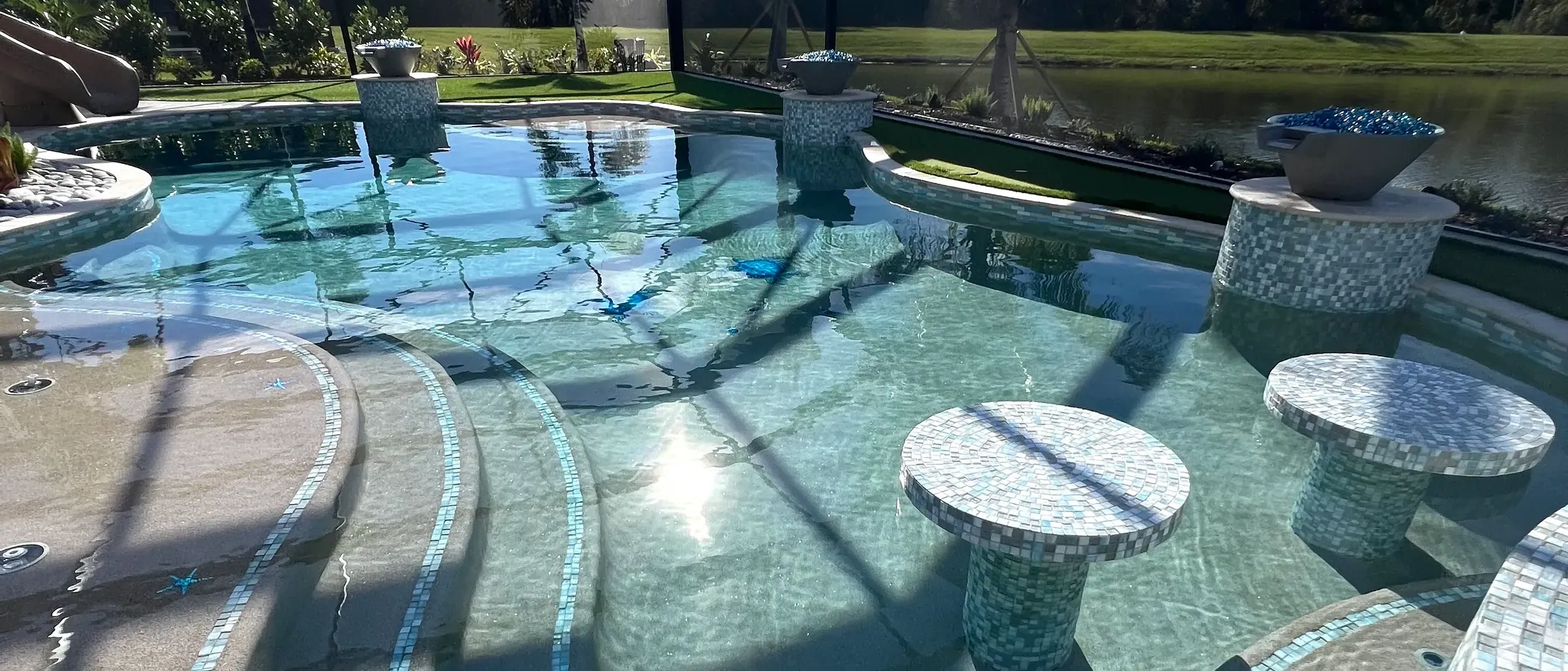 Freeform lagoon pool and spa with in-pool seating, large sun shelf, water and fire features, turf and a large screen enclosure